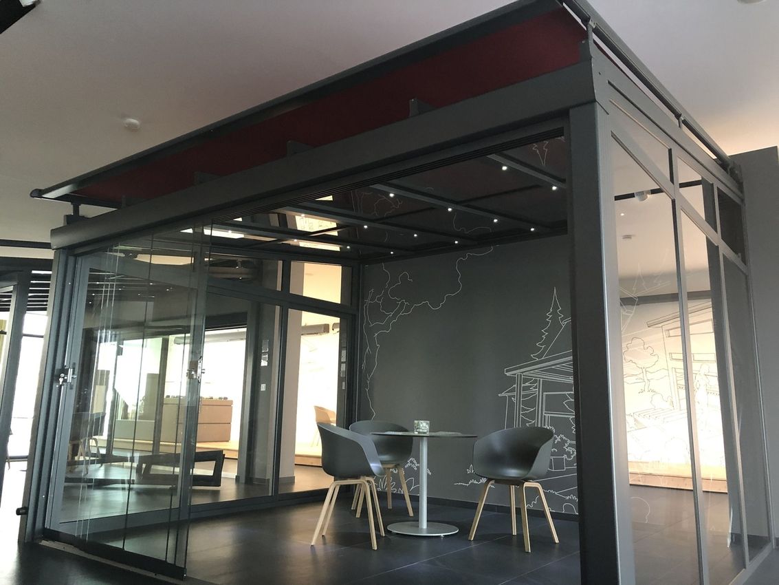 Moderner Pavillon mit Glaswänden, zwei Stühlen und einem kleinen Tisch im Inneren