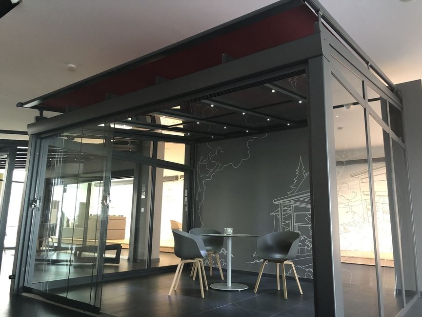 Moderner, schwarzer Pavillon mit Glaswänden, darin zwei Stühle und ein runder Tisch