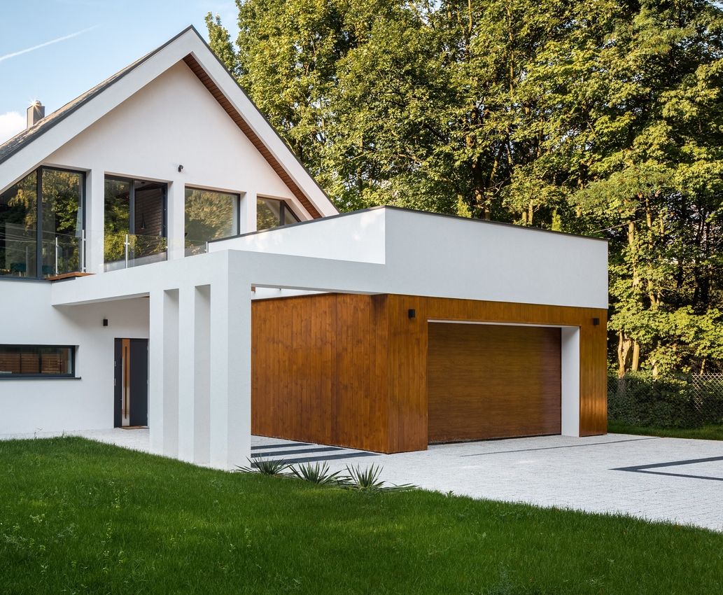 Modernes Einfamilienhaus mit weißer Fassade, Flachdach-Garage mit Holztor und großem Fenster im Obergeschoss, umgeben von Bäumen