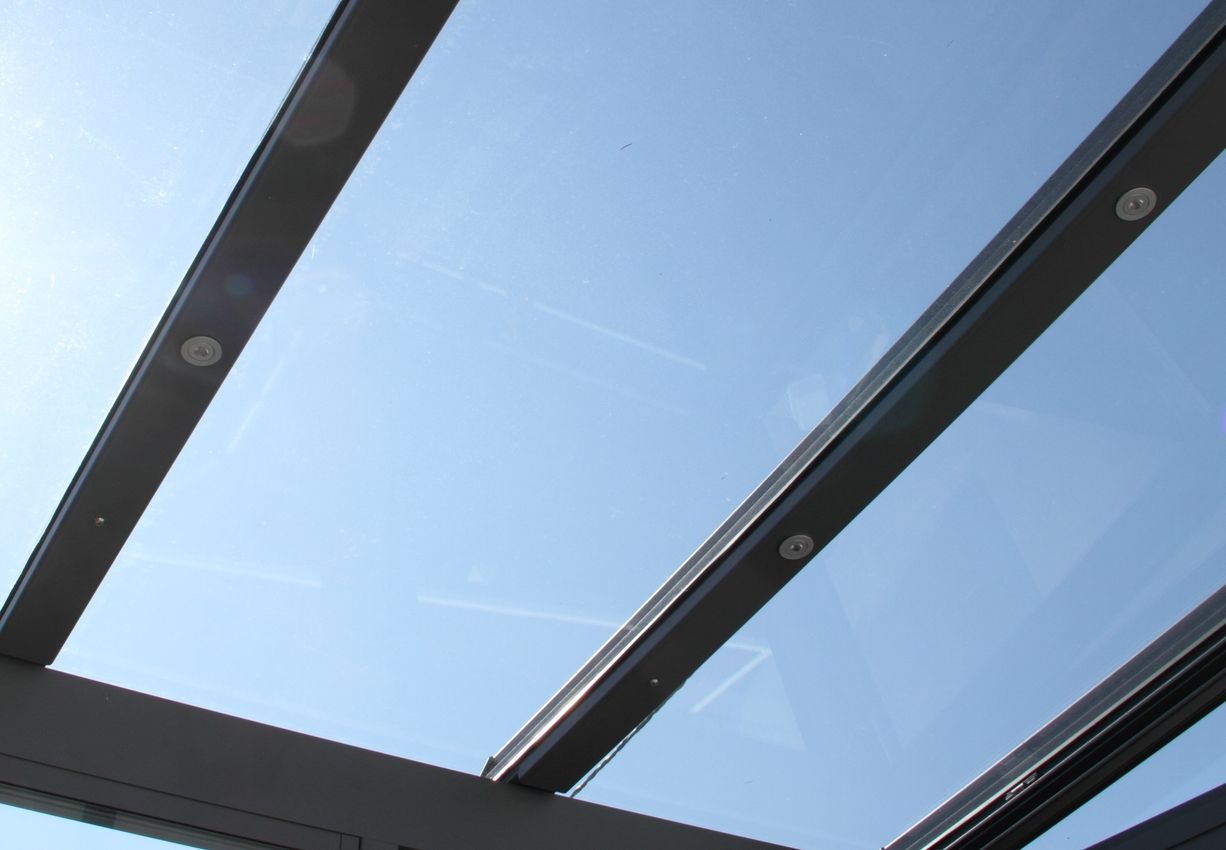 Blick durch ein Glasdach mit sichtbaren Metallstreben vor blauem Himmel