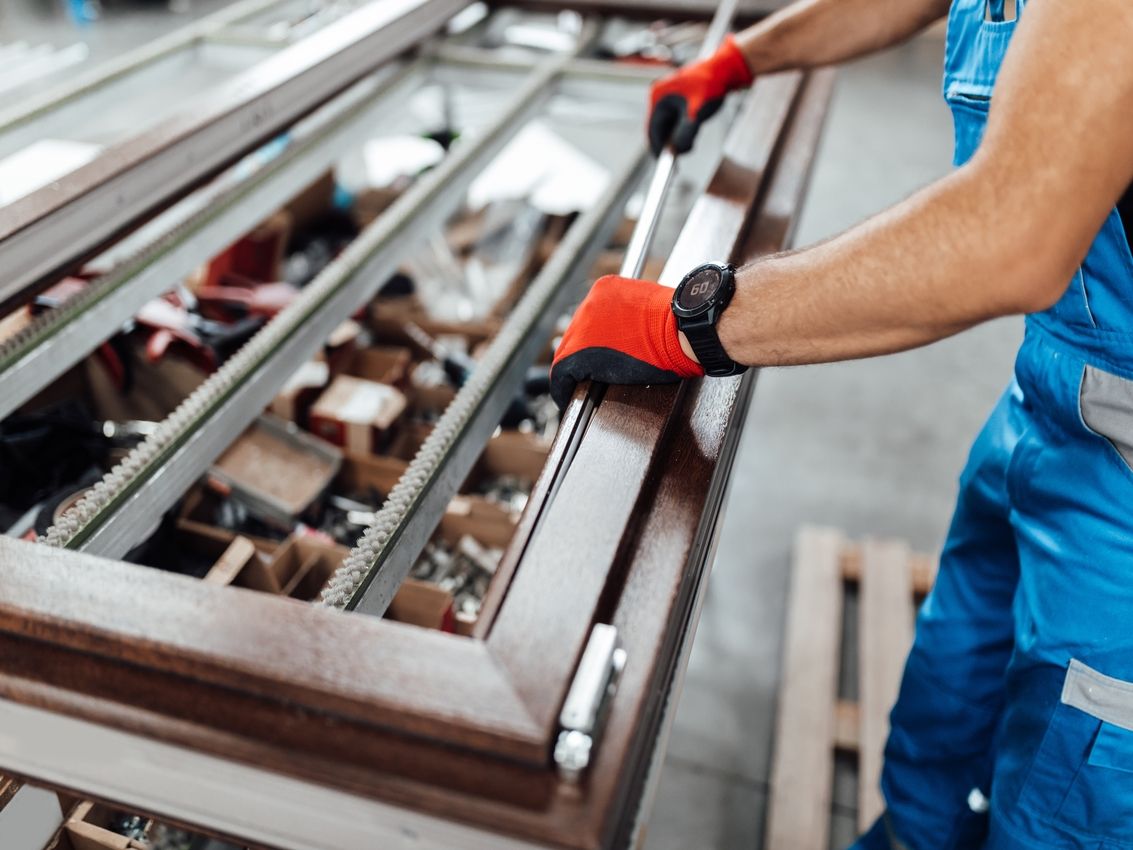Fassade eines Gebäudes mit vertikalen Metallpaneelen und zwei rechteckigen, leicht geöffneten Fenstern mit Außenjalousien unter blauem Himmel mit Wolken