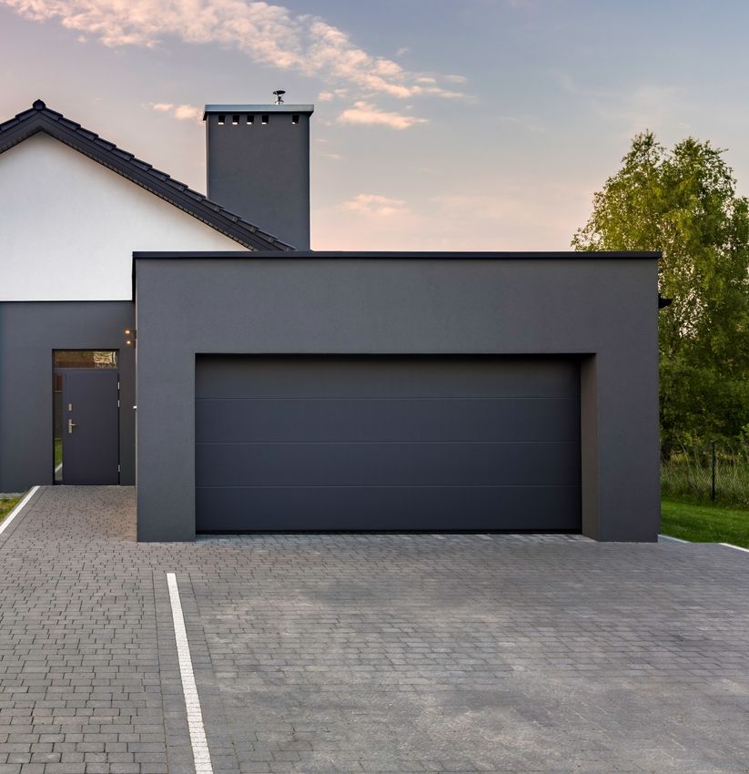 Modernes Einfamilienhaus mit flacher Garage und gepflasterter Einfahrt vor bewölktem Himmel